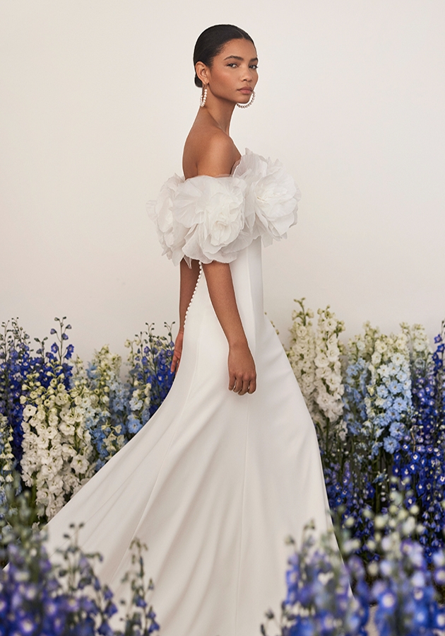 Romantic two-piece sheath-style wedding dress, made in crêpe. Featuring a strapless neckline and detachable cuff with organza flowers. Impress in a delicate Rosa Clará Couture gown.