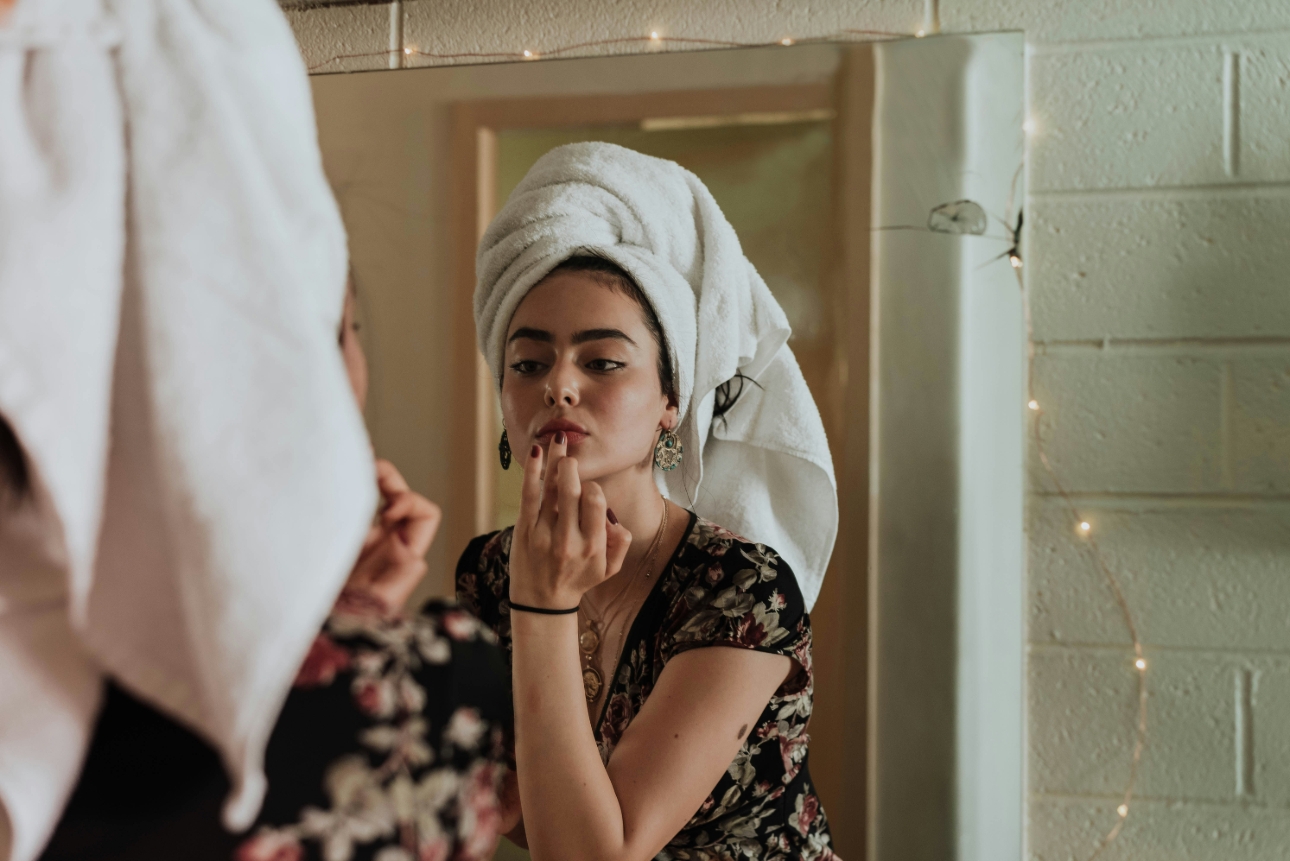 woman looking in mirror applying lip balm 